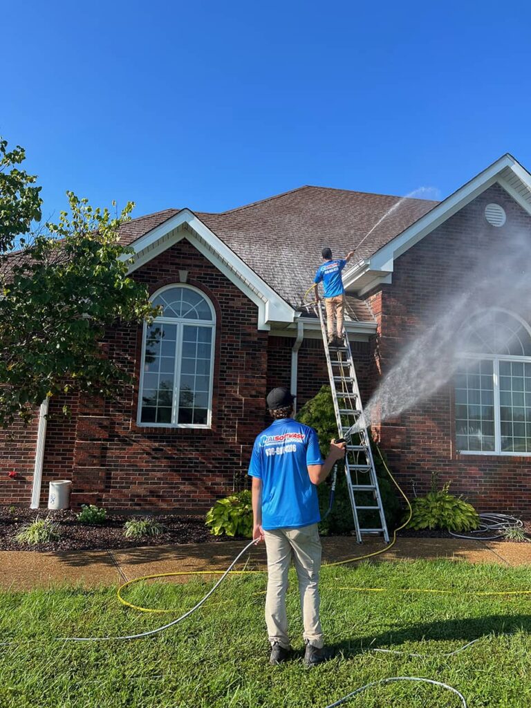 Total Softwash Solutions professionals washing brick home with professional standing on ladder washing roof