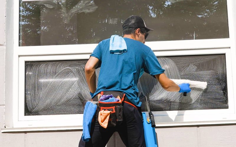 window cleaning professional in blue shirt cleaning windows with soap brush